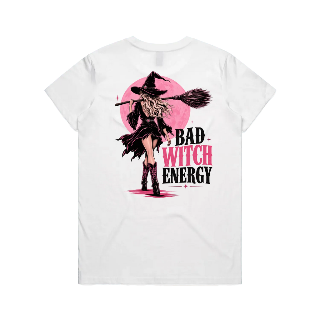 A white short-sleeve t-shirt shown from the back, featuring a graphic print of a witch with a broomstick in front of a pink moon, with the text 'BAD WITCH ENERGY' in black and pink.